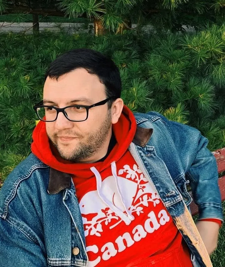 Photo of Goran sitting on a park bench surrounded by greenery in Waterloo, Ontario, Canada.
