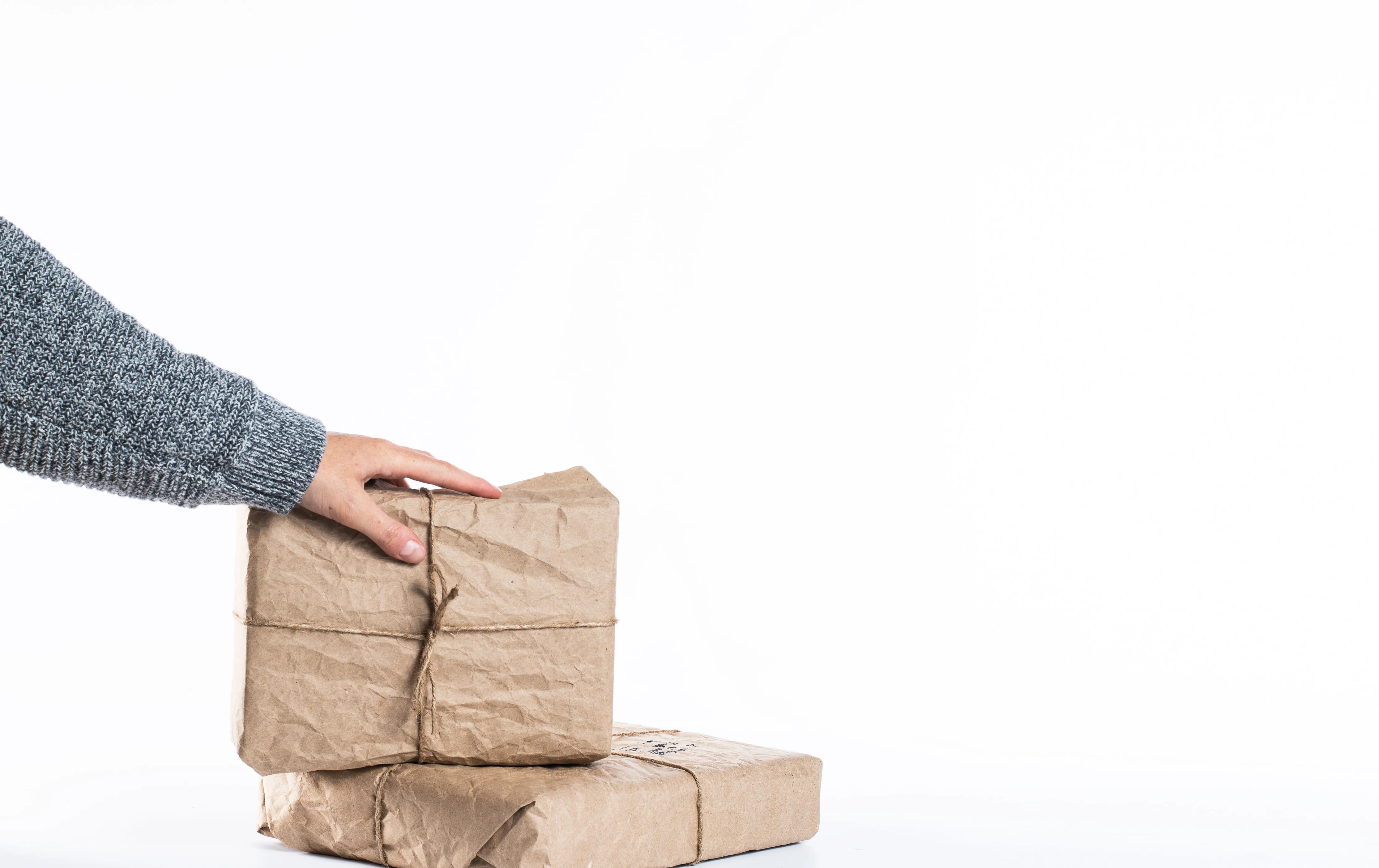 Person standing out of frame stacking mail packages on a white background.
